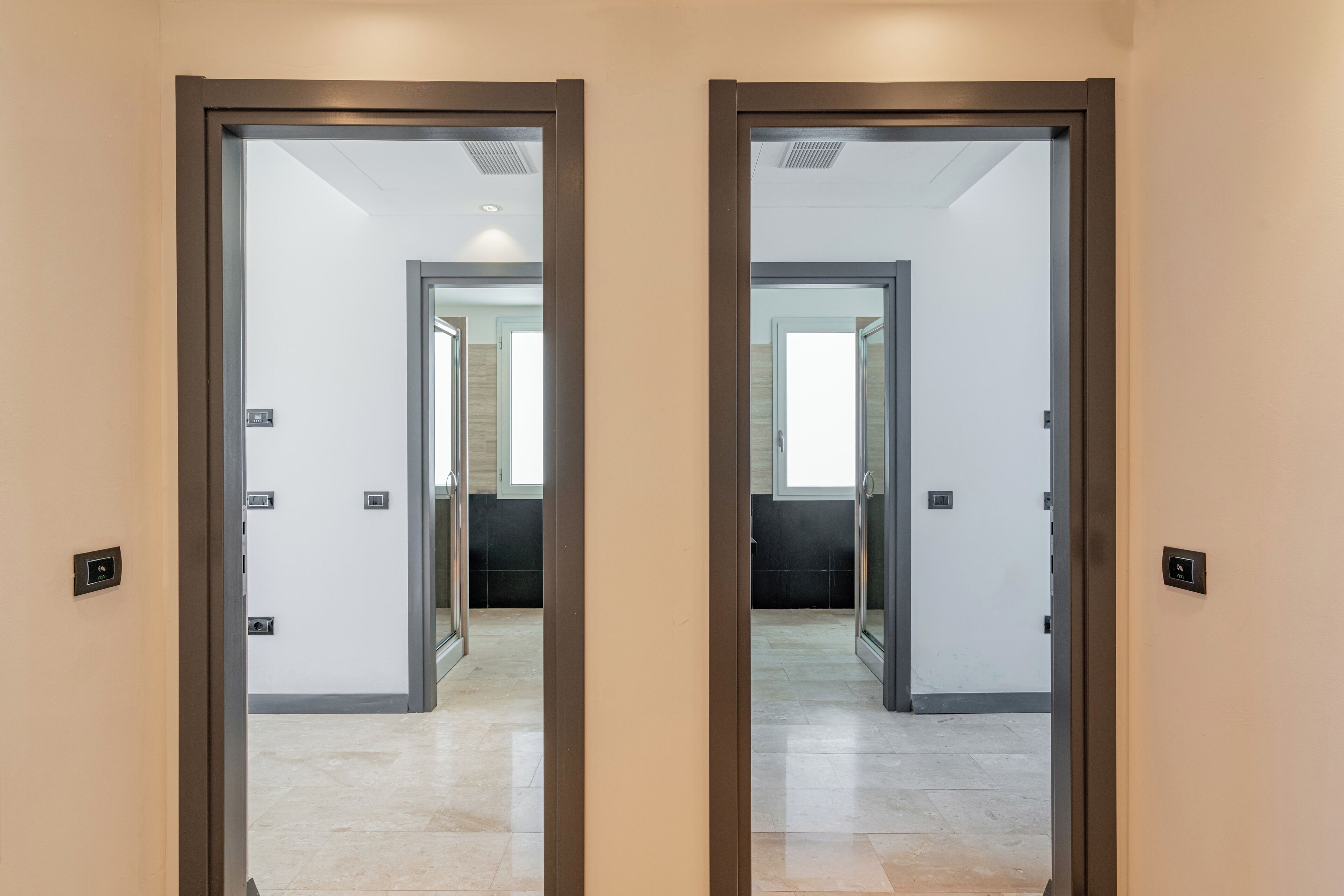 A hallway with two mirrored doors leading to a room with a tiled floor and a window.
