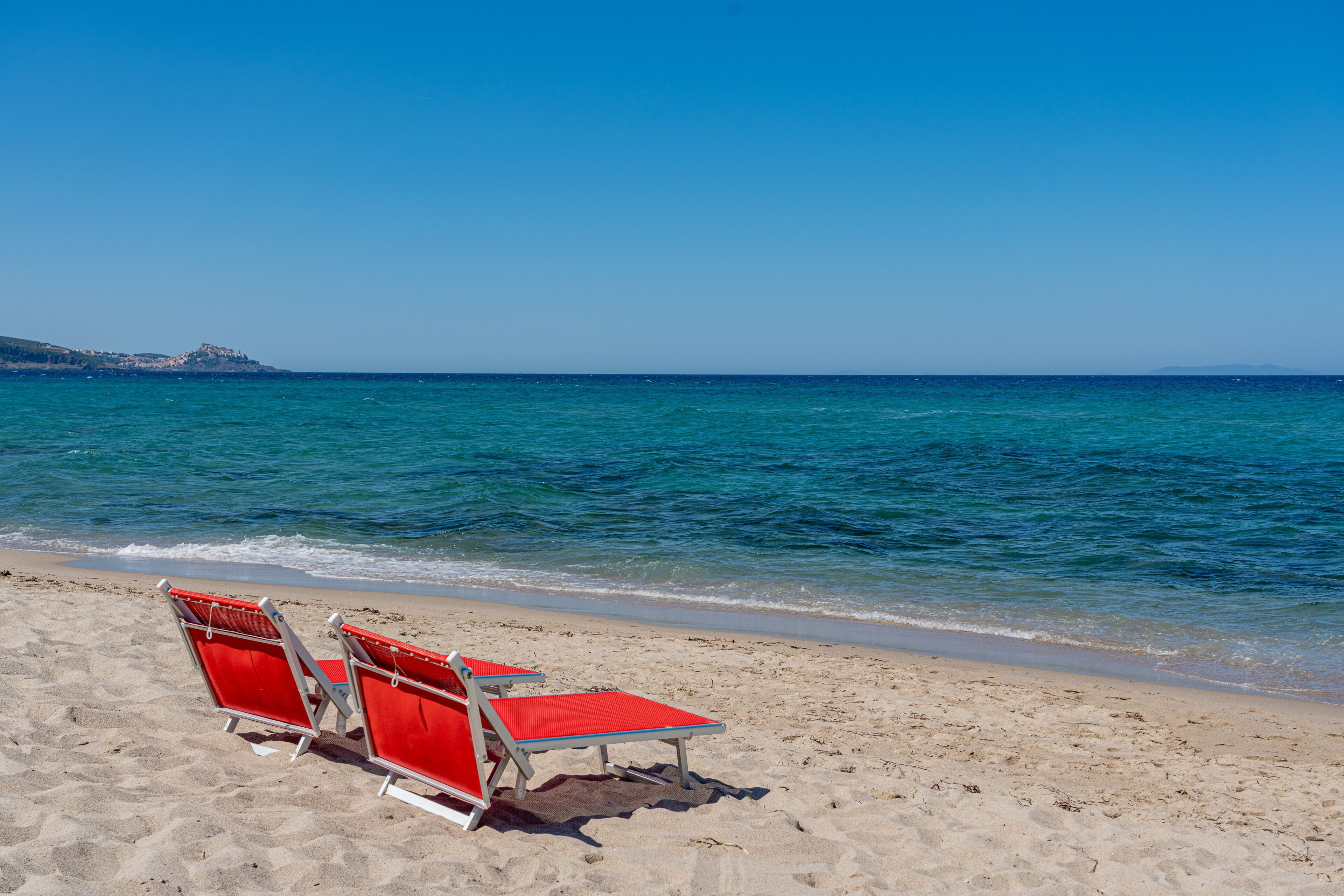 Une plage avec trois chaises longues rouges et une vue dégagée sur l’océan.