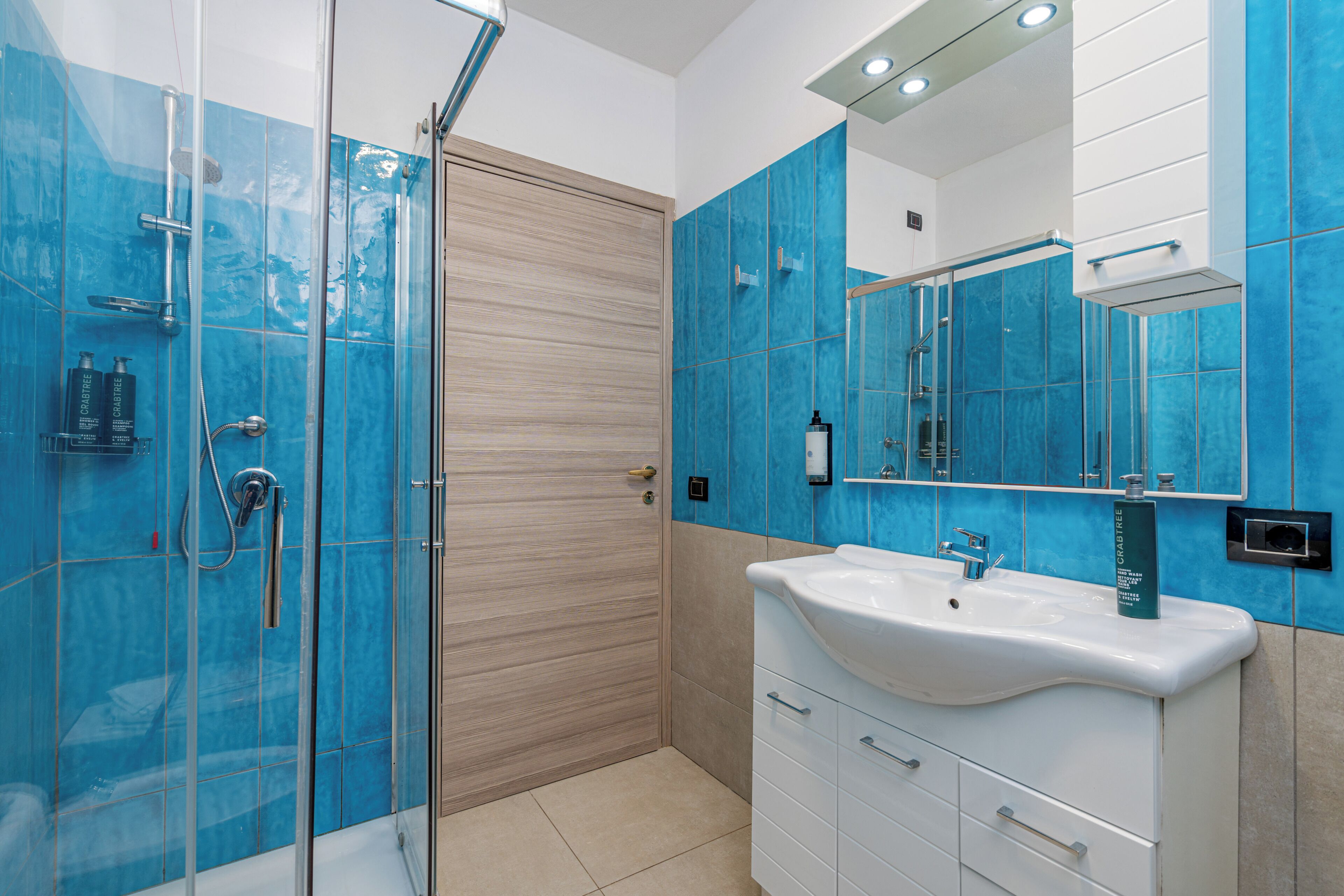 A modern bathroom with a glass shower enclosure, a white sink, and blue-tiled walls.