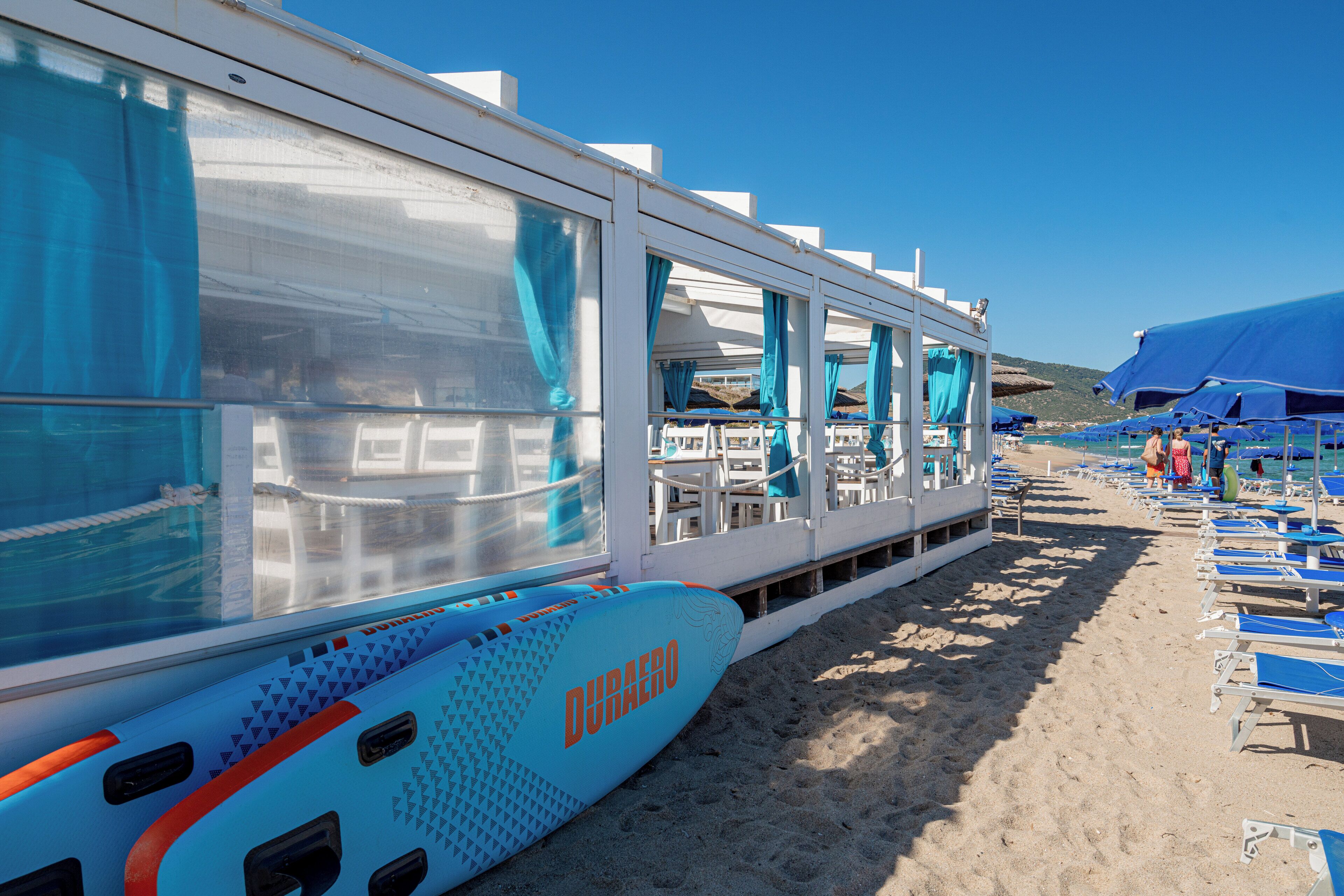 Een cruiseschip aan de kust met een blauw-wit kleurenschema, voorzien van buitenzitplaatsen en parasols.
