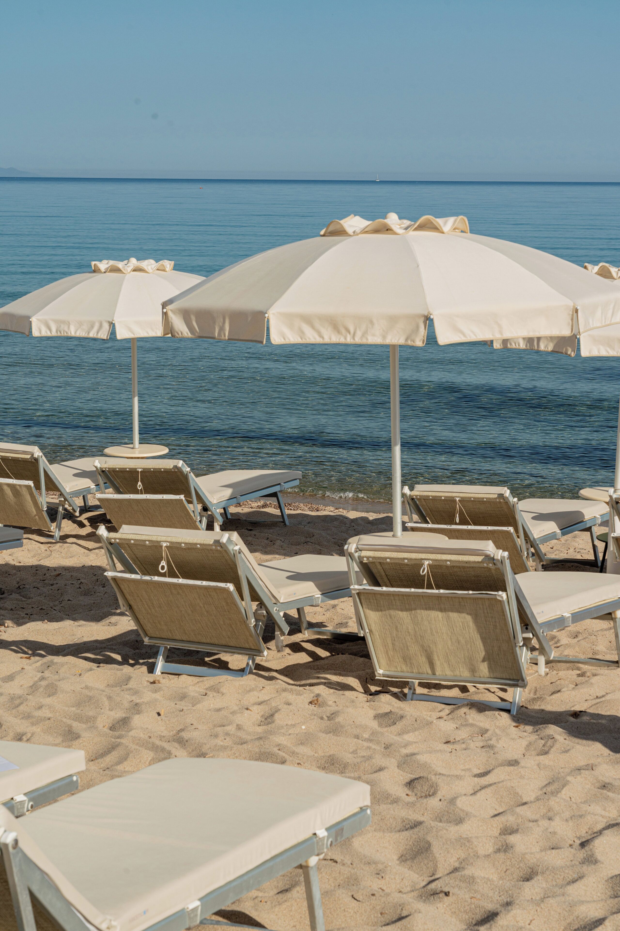 Beach chairs and umbrellas arranged on a sandy beach with a view of the sea.