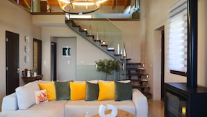 A modern living room with a sectional sofa, a round wooden coffee table, a fireplace, and a staircase with glass railings. - Villa ArGia with private pool & sea view (Apokoronas)