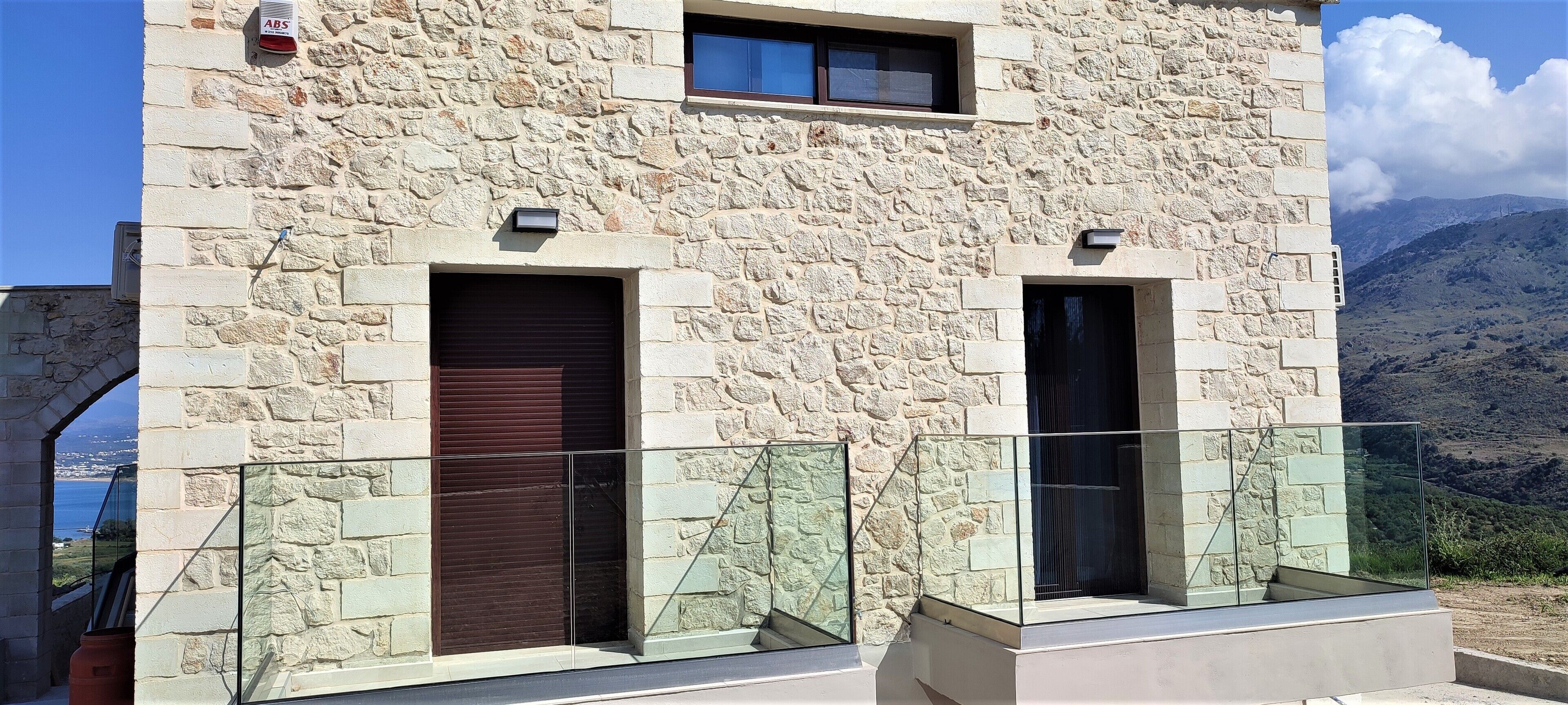Um edifício de pedra com duas portas fechadas e uma varanda com grades de vidro.