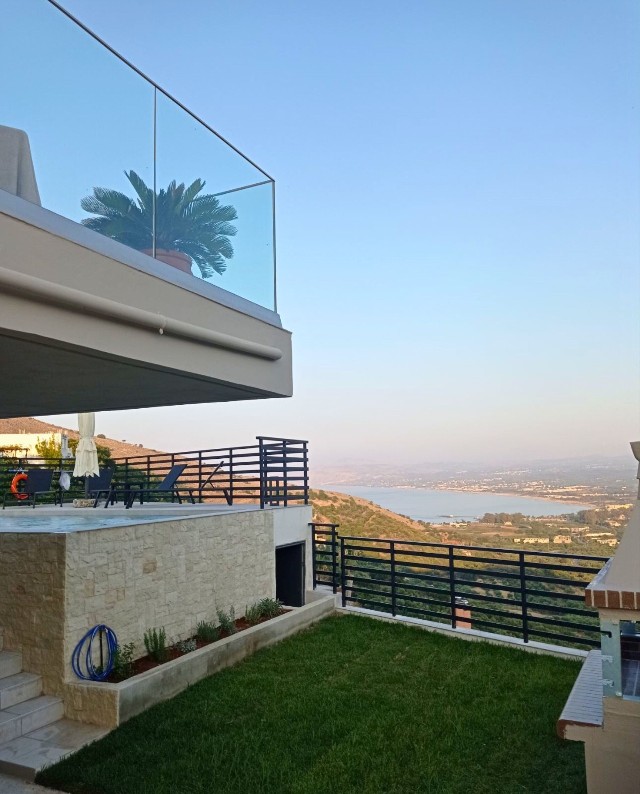 A modern outdoor area with a pool, lounge chairs, and a view of a lake and distant cityscape.