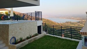 A modern outdoor area with a pool, lounge chairs, and a view of a lake and distant cityscape. - Villa ArGia with private pool & sea view (Apokoronas)