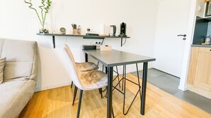 Un espacio habitable compacto con una mesa de comedor, un sillón acolchado, un sofá y una cocina equipada con cafetera y utensilios.