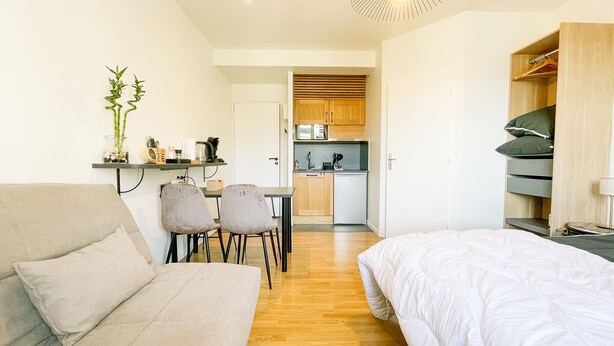 Una habitación compacta con cama, sofá, mesa de comedor con sillas, kitchenette y armario.