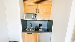 Una cocina compacta con armarios de madera, un lavamanos de acero inoxidable, un microondas y un lavavajillas.