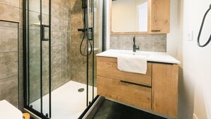 Un baño moderno con ducha envuelta en vidrio, tocador de madera con lavabo blanco y un espejo grande sobre el tocador.