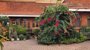A courtyard with a brick building, potted plants, and a variety of flowering plants. - Orchid Gardens; Studio Apartment, minimalist (Kampala)