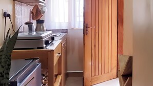A kitchen with wooden cabinets, a countertop, and a window with curtains. - Orchid Gardens; Studio Apartment, minimalist (Kampala)
