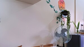 A modern living room with a wooden table set for two, a sofa, a small white side table, and a decorative wall piece. - Orchid Gardens; Studio Apartment, minimalist (Kampala)