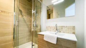 Een moderne badkamer met een douche met glazen wand, een witte wastafel en een houten meubel.