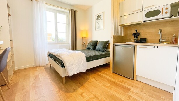 Een knus slaapkamer met een bed, nachtkastje en een klein bureau. Grenzend daar aan bevindt zich een kitchenette met een magnetron, gootsteen en bergkasten.