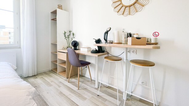 A minimalist bedroom with a bed, a desk with a chair, a stool, and a mirror on the wall. - #GB | Au Coeur de l'Essentiel 2 🈴 (Saint-Martin-le-Vinoux)