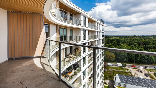 Un edificio de varios pisos con balcones, ventanas amplias y vistas a un paisaje verde.