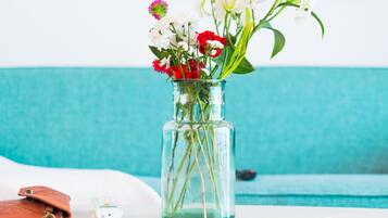 Un vase en verre transparent, orné de fleurs, est posé sur une table blanche dans une pièce aux murs de couleur turquoise, avec une peinture abstraite et colorée en arrière-plan.