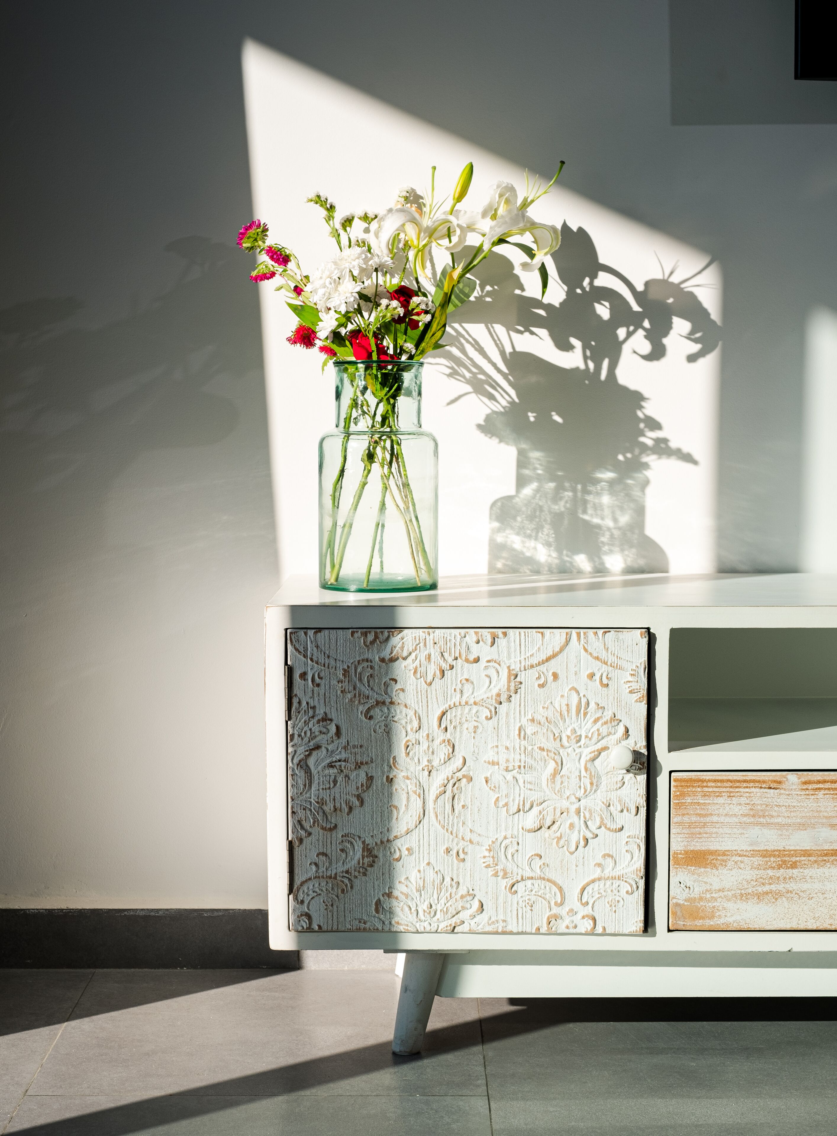 Un vaso di vetro trasparente con fiori su un mobile bianco decorato.