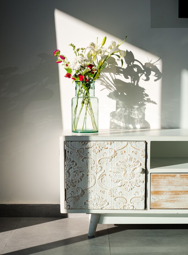 A clear glass vase with flowers on a white cabinet with a decorative pattern. - Asilah 32 (Asilah)