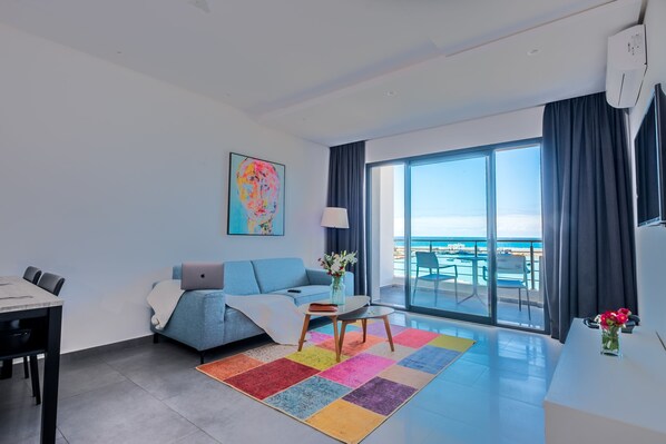 Una sala de estar moderna con un sofá, una mesa de comedor y vista al mar a través de amplios ventanales.