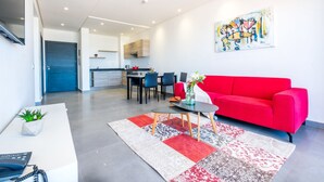 A modern living room with a red sofa, a coffee table, and a patterned rug. There is a dining area with chairs and a table, and a kitchen in the background. - Asilah 32 (Asilah)