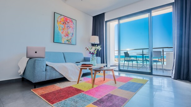 A modern hotel room with a large balcony, a laptop on the bed, a colorful rug, and a painting on the wall. - Asilah 32 (Asilah)