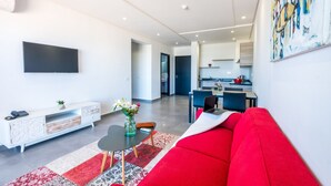 A modern living room with a red sofa, a flat-screen TV, a white console, and a dining area in the background. - Asilah 32 (Asilah)