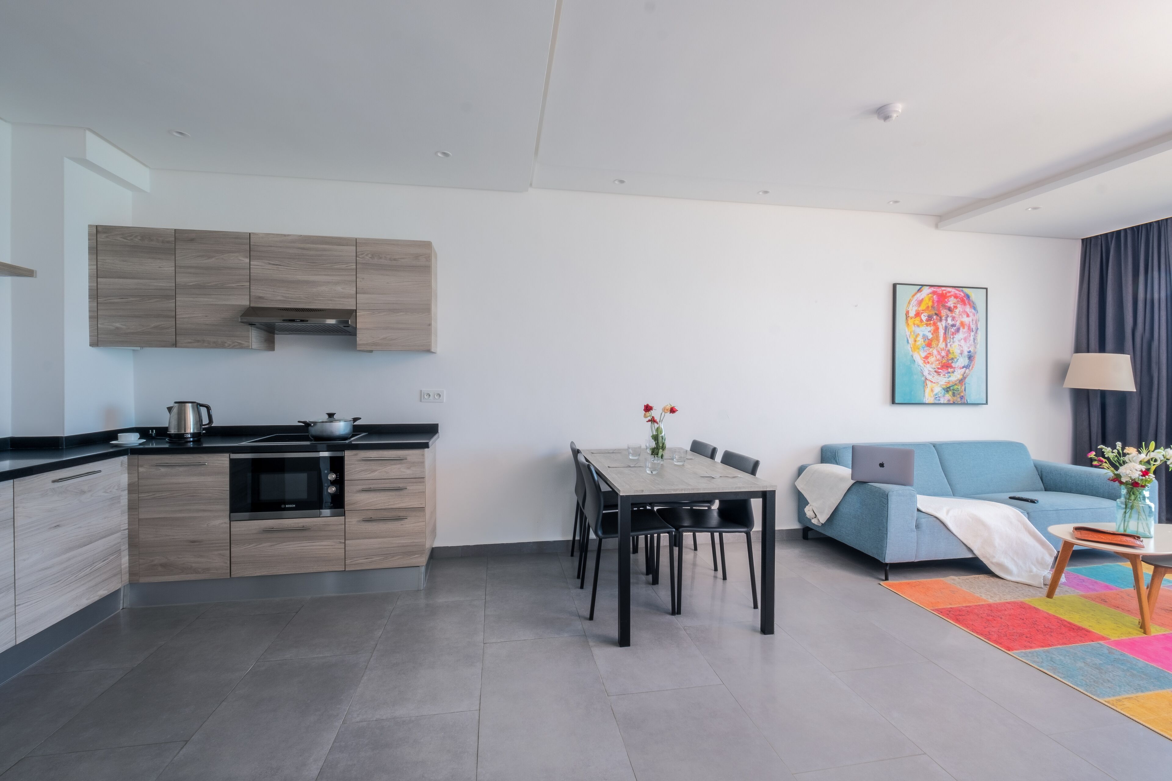 Una cucina moderna con mobili in legno, un tavolo da pranzo con sedie, un divano e un tappeto colorato.
