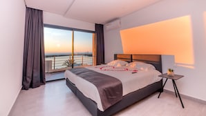 A modern hotel room with a large bed, a small bedside table, and a view of the sunset over the water. - Asilah 32 (Asilah)