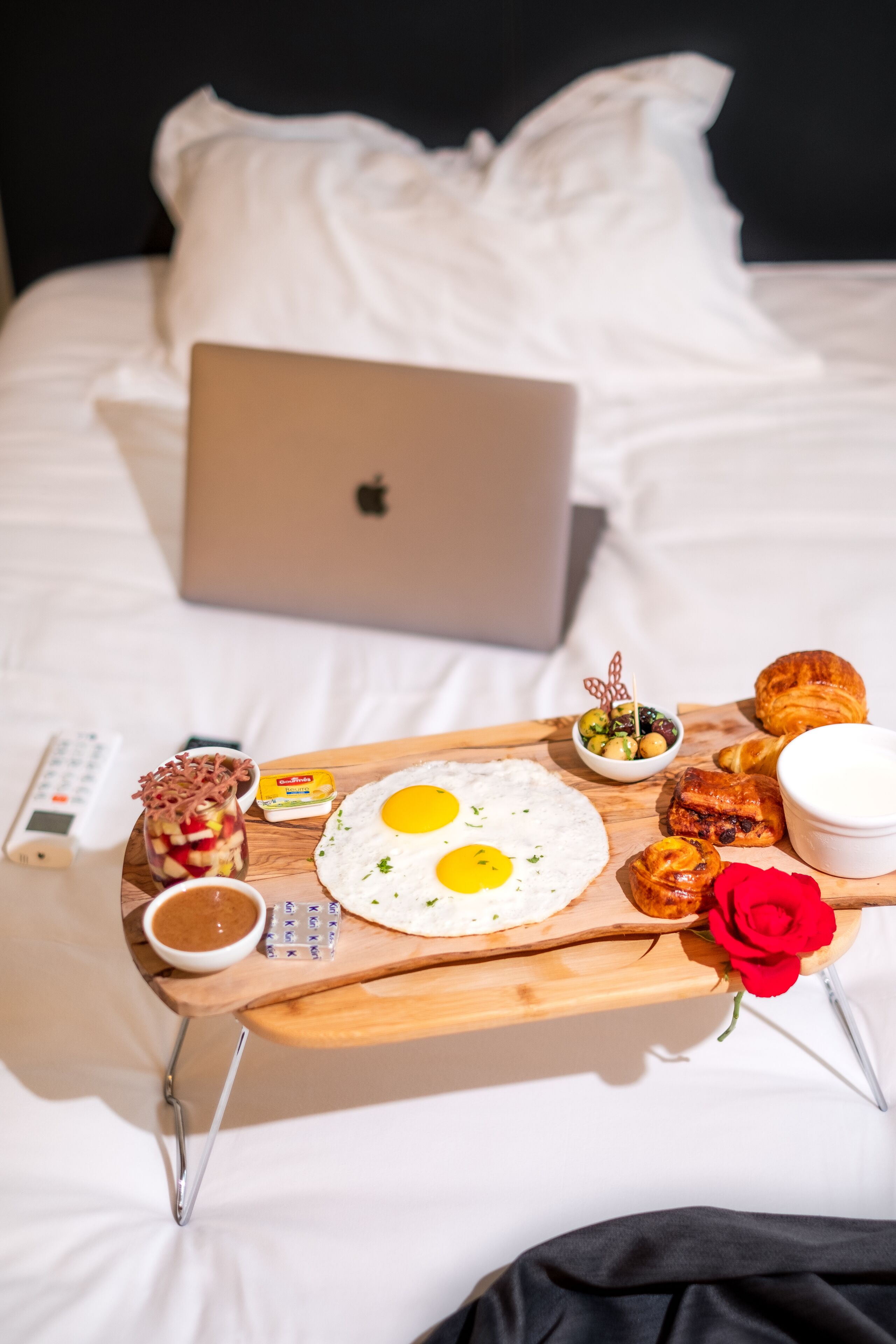 Ein Bett mit einem Laptop, einem Tablett mit Speisen und einer Rose.