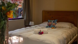 Una cama bien tendida con ropa blanca, un cabecero de madera y una almohada decorativa.
