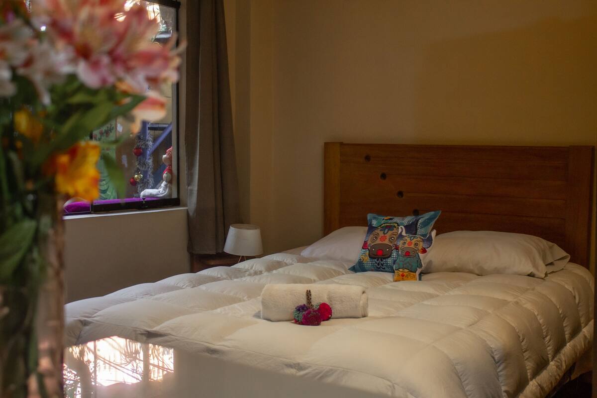 Una cama bien tendida con ropa blanca, un cabecero de madera y una almohada decorativa.