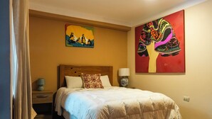 Habitación de hotel con cama, mesita de noche, lámpara y dos cuadros en la pared.
