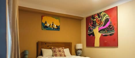 Habitación de hotel con cama, mesita de noche, lámpara y dos cuadros en la pared.