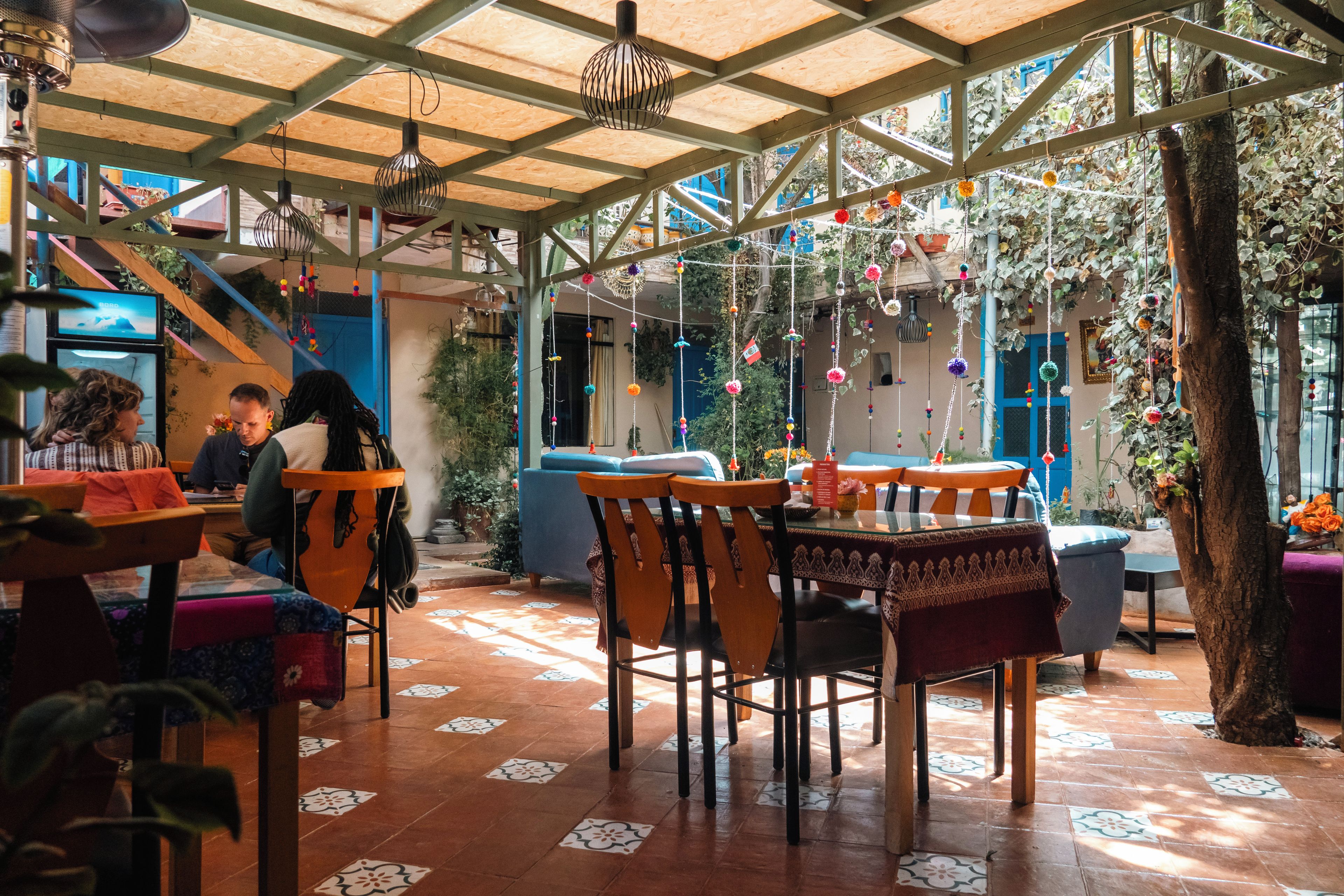 An indoor dining area with wooden tables and chairs, a tiled floor, and a wooden ceiling structure.