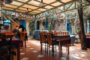 Un comedor interior con mesas y sillas de madera, suelo de baldosas y estructura de techo de madera.