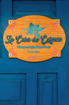 Un letrero de madera con el texto 'La Casa de Carmen Hospedaje Familiar' sobre un fondo azul.