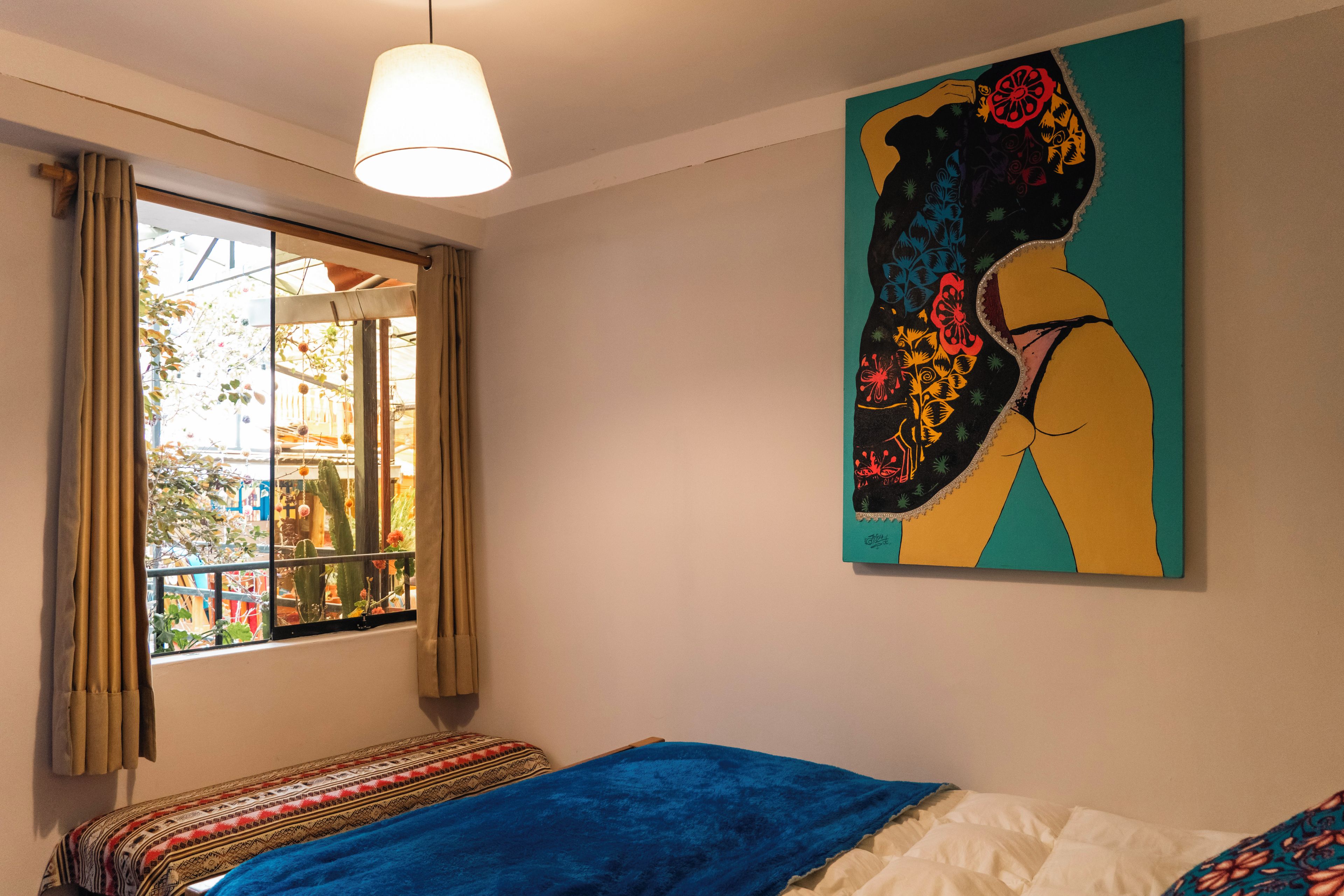 Un dormitorio con una cama, una ventana con cortinas, una lámpara colgante y una obra de arte colorida en la pared.