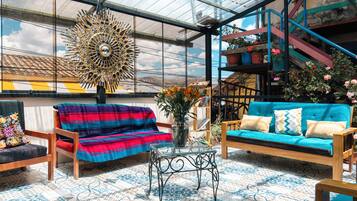 Una habitación amplia con un gran techo de vidrio, un banco tejido de colores, un sofá azul y una escalera con barandillas coloridas.