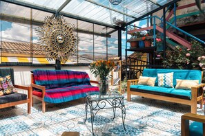Una habitación amplia con un gran techo de vidrio, un banco tejido de colores, un sofá azul y una escalera con barandillas coloridas.