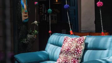 Un sofá azul con un cojín estampado en una habitación con adornos colgantes y una pared rústica.