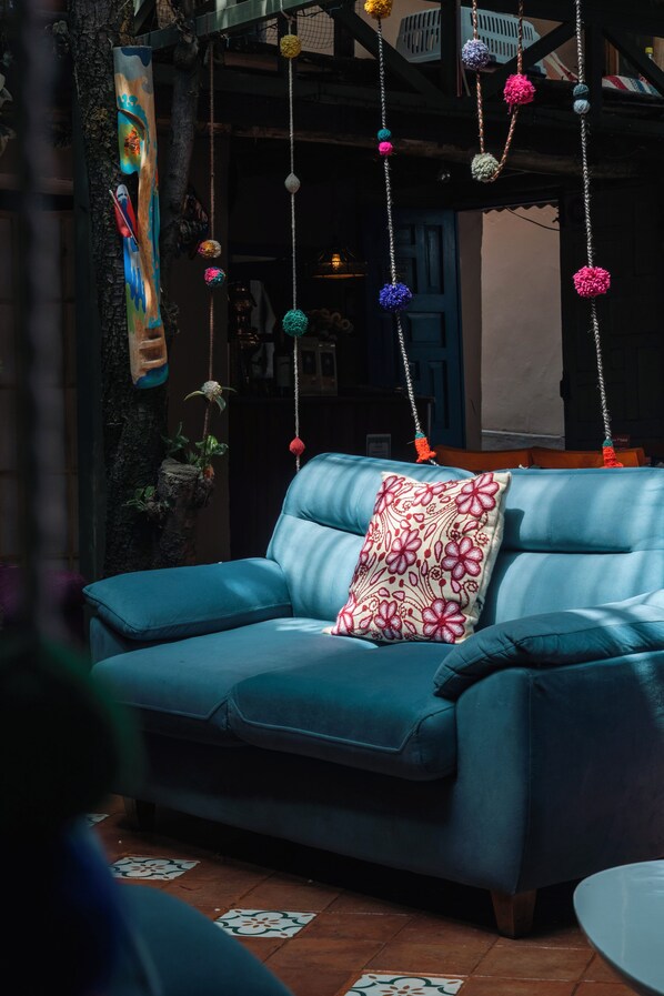 Un sofá azul con un cojín estampado en una habitación con adornos colgantes y una pared rústica.