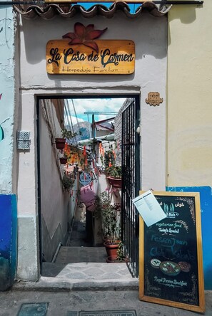 Ein schmaler Gang, der zu einem Gebäude führt, an dem ein Schild mit der Aufschrift 'La Casa de Carmen Hospedaje Familiar' befestigt ist.
