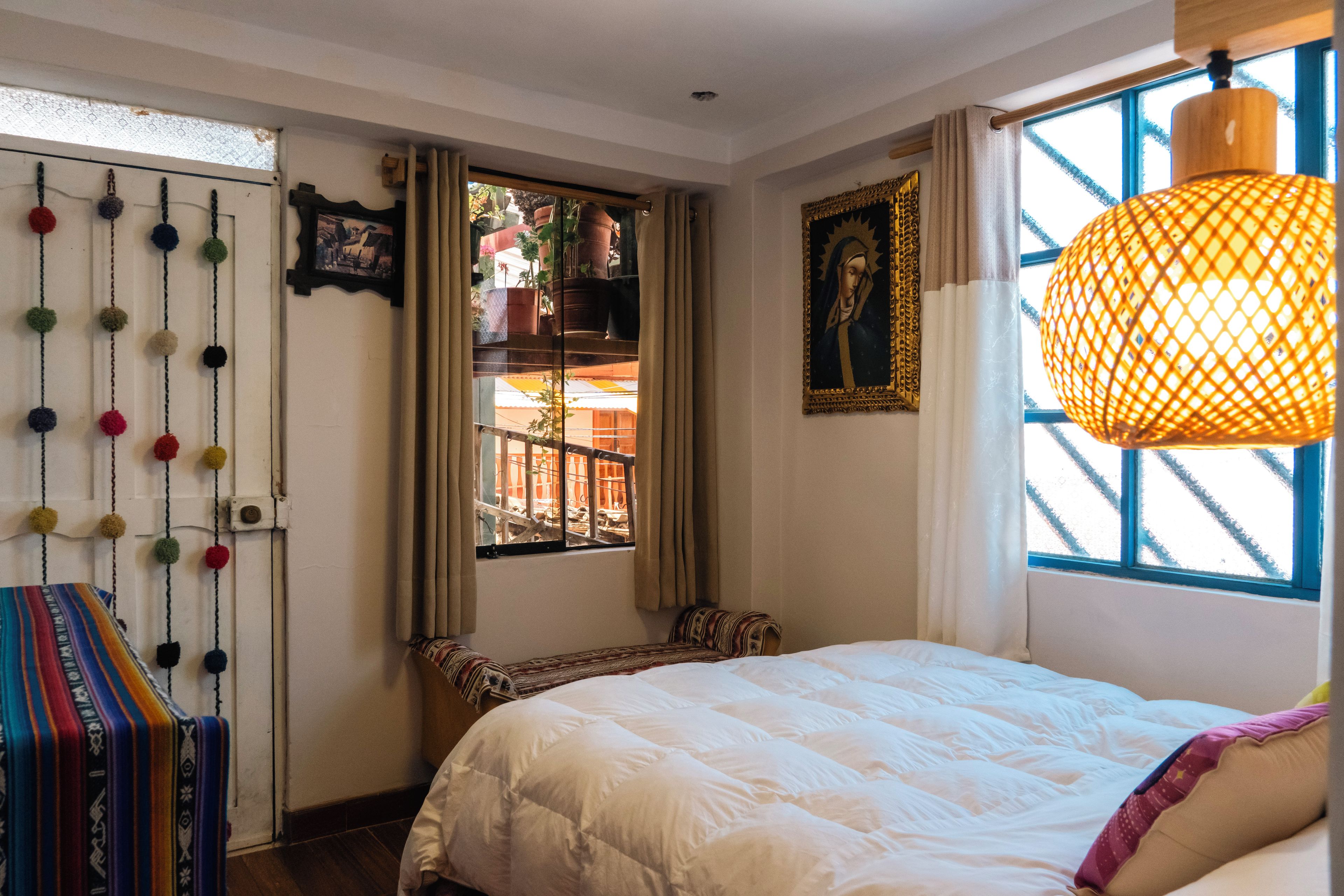 Un dormitorio con cama, ventana con cortinas, planta colgante y un cuadro en la pared.