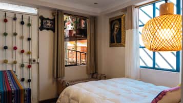 Un dormitorio con cama, ventana con cortinas, planta colgante y un cuadro en la pared.