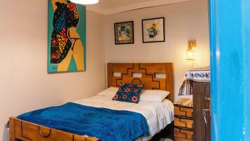 Un dormitorio con cabecera de madera, cama con manta azul, lámpara colgante y dos cuadros en la pared.