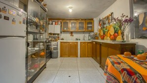 Una cocina con refrigerador, armarios y una mesa de comedor con mantel colorido.