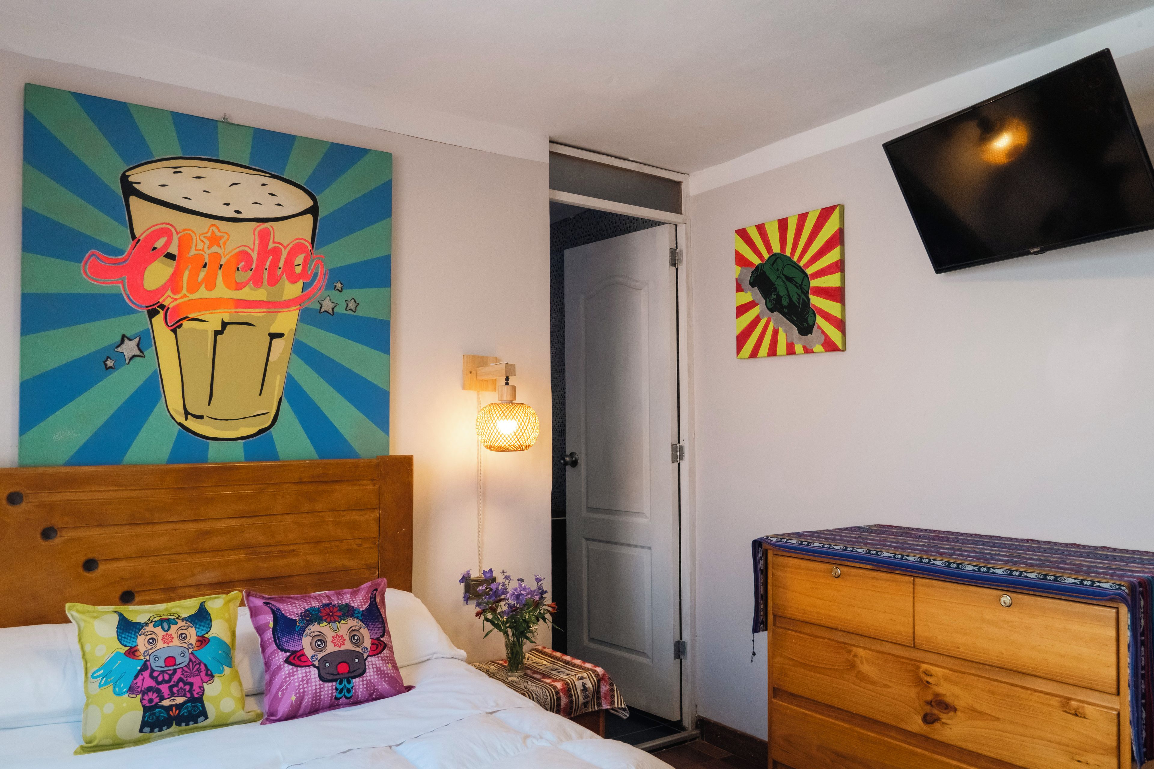 Una habitación de hotel con una cama, un aparador de madera, un televisor en la pared y dos cuadros.