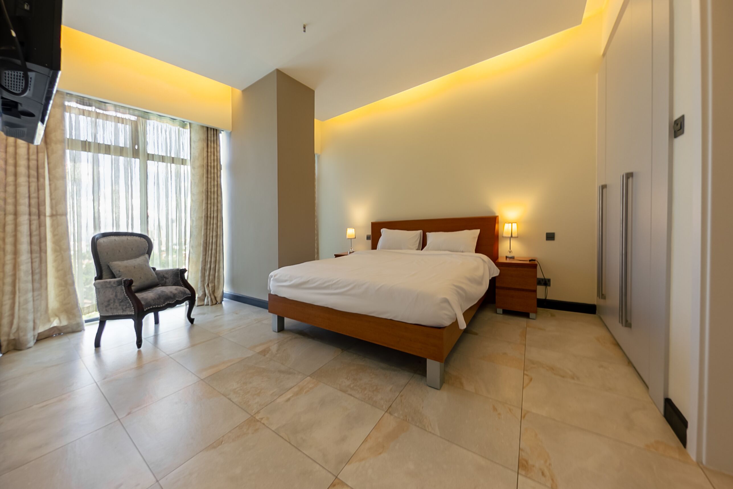 A modern hotel bedroom with a large bed, a chair, and a nightstand.