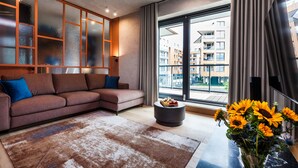 A modern living room with a sectional sofa, a round coffee table, and a large window with a city view. - Brabank Residence by HappyStay (Gdansk)